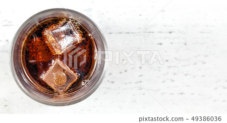 Tabletop view, glass with cola drink and ice cubes on white board. Wide photo, space for text right. Tabletop view, glass with cola drink and ice cubes on white board. Wide photo, space for text right. 49386036