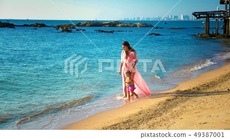 blonde Baby crawling on the sandy beach, mom happily looks at her 49387001