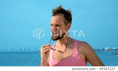 Playful handsome guy in a pink t-shirt and blue shorts rejoices at the beach. freak on the sea. 49387227