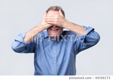 Senior happy man in blue shirt covering eyes Senior happy man in blue shirt covering eyes 49388173