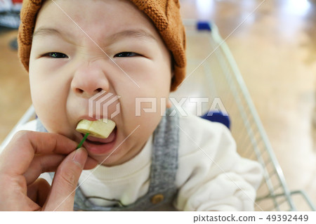 A baby boy sitting in a shopping cart eating a banana A baby boy sitting in a shopping cart eating a banana 49392449