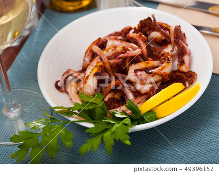 Delicious cooked squid or octopus tentacles with lemon and parsley on a plate 49396152