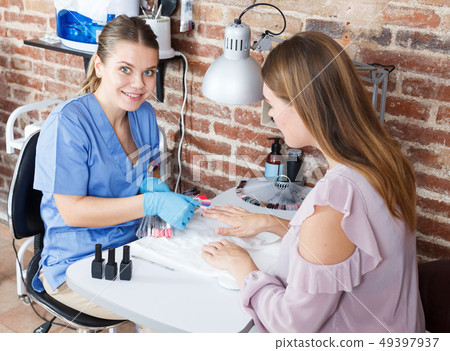 Manicurist doing procedure of manicure nail to woman client in salon Manicurist doing procedure of manicure nail to woman client in salon 49397937
