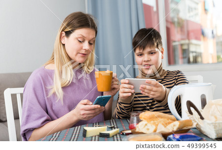 Portrait of young mother and son using phones during breakfast 49399545
