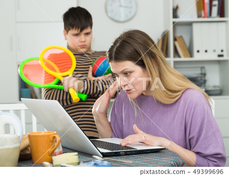 Son asking busy mother playing with racquets for tennis, she working 49399696