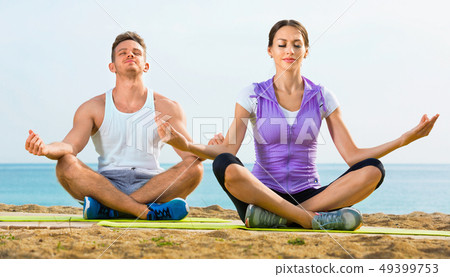 Woman and man sitting cross-legged do yoga poses on beach Woman and man sitting cross-legged do yoga poses on beach 49399753