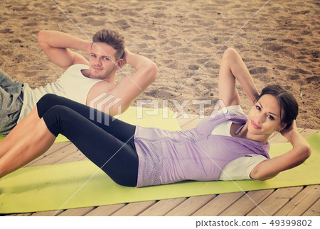 Young man and girl training on beach by ocean Young man and girl training on beach by ocean 49399802
