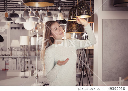 Woman looking pendent lamp in furniture showroom Woman looking pendent lamp in furniture showroom 49399938
