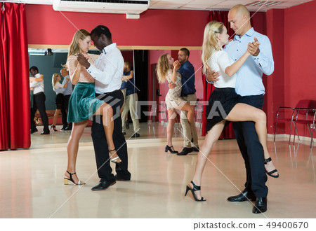 Portrait of positive adult pairs enjoying tango in modern dance hall Portrait of positive adult pairs enjoying tango in modern dance hall 49400670