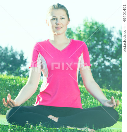 Adult female in pink T-shirt is sitting and meditating Adult female in pink T-shirt is sitting and meditating 49401491