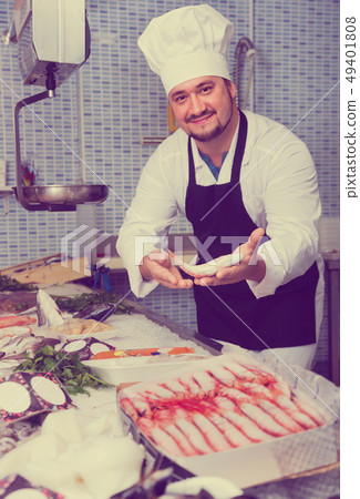 Seller in white cap and black apron showing counter with fish Seller in white cap and black apron showing counter with fish 49401808