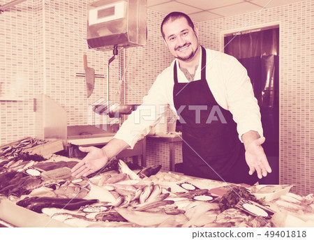 Seller in black apron showing fish on his counter Seller in black apron showing fish on his counter 49401818