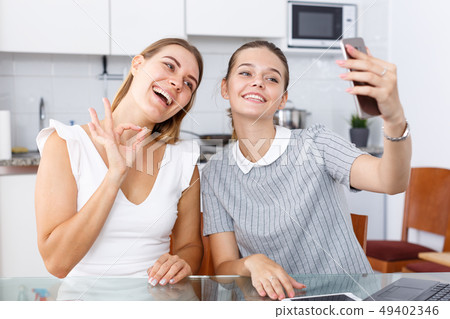 Two young girlfriends making selfie by phone and smiling at table Two young girlfriends making selfie by phone and smiling at table 49402346