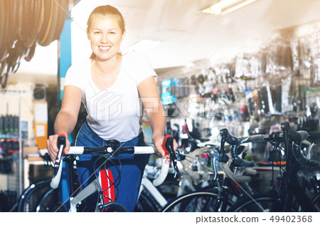 Portrait of girl who is standing with bicycle in store. 49402368