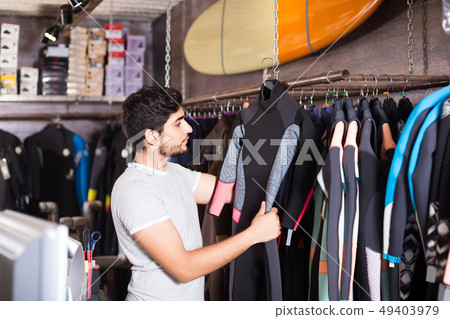 man holding and choosing suit for surfing in the shop 49403979