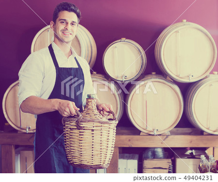 man in uniform holding large wine bottle with wicker and standin 49404231