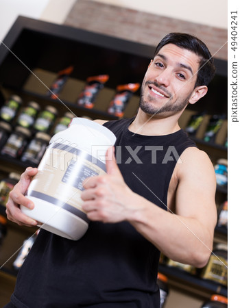 Attractive sport man holding thumb up and pot of sport supplements Attractive sport man holding thumb up and pot of sport supplements 49404241