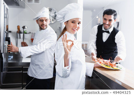 Smiling woman chef approving dish in kitchen of fish restaurant before serving guests Smiling woman chef approving dish in kitchen of fish restaurant before serving guests 49404325