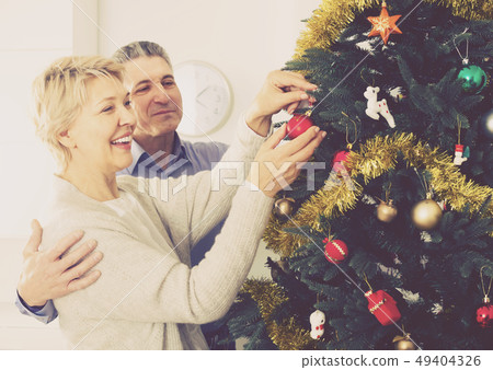 Mature smiling couple decorate fir-tree for holidays of Christmas and New Year Mature smiling couple decorate fir-tree for holidays of Christmas and New Year 49404326