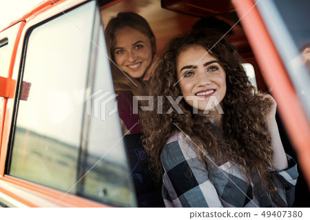 Young female friends on a roadtrip through countryside, looking out of minivan. 49407380