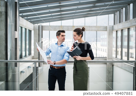 Two young architects with blueprints standing in office, talking. Two young architects with blueprints standing in office, talking. 49407881