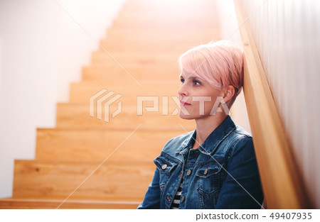 A young attractive woman sitting at the bottom of the stairs at home. A young attractive woman sitting at the bottom of the stairs at home. 49407935
