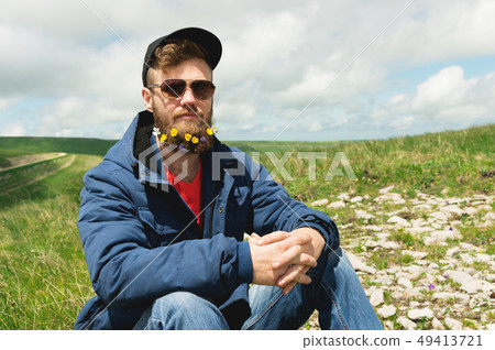 Portrait of a cheerful bearded man in sunglasses and a gray cap with wildflowers in a beard. Soft Portrait of a cheerful bearded man in sunglasses and a gray cap with wildflowers in a beard. Soft 49413721