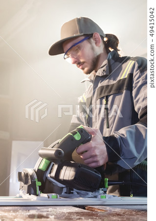 Portrait of a young carpenter joiner with manual circular power saw in the hands of a worker in a 49415042