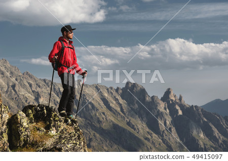 Porter of a bearded traveler hipster in sunglasses and a cap with a backpack and trekking poles Porter of a bearded traveler hipster in sunglasses and a cap with a backpack and trekking poles 49415097