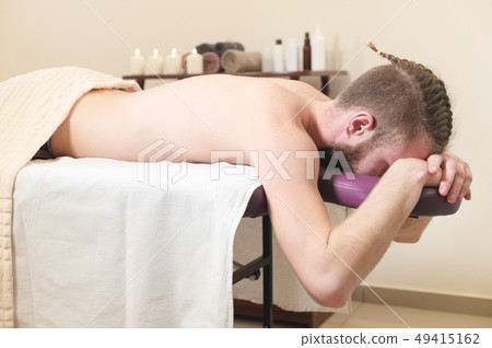Male hipster with braided trendy hair and shaved temples lying on a massage bunk down face resting Male hipster with braided trendy hair and shaved temples lying on a massage bunk down face resting 49415162