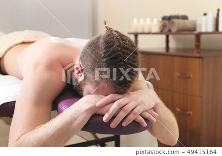Male hipster with braided trendy hair and shaved temples lying on a massage bunk down face resting Male hipster with braided trendy hair and shaved temples lying on a massage bunk down face resting 49415164