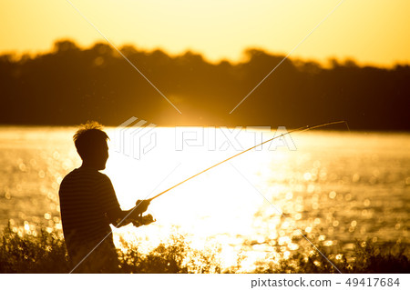 Fisherman with a fishing rod at sunset 49417684
