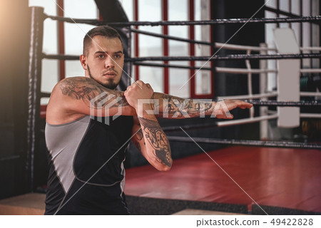 Working his core muscles. Young muscular athlete in sports clothing looking away while warming up Working his core muscles. Young muscular athlete in sports clothing looking away while warming up 49422828