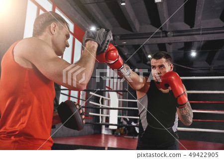 Heavy blow to the head. Strong tattooed athlete in sports clothing training on boxing paws with Heavy blow to the head. Strong tattooed athlete in sports clothing training on boxing paws with 49422905