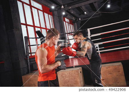 Knockout punch. Strong tattooed athlete in sports clothing training on boxing paws with partner Knockout punch. Strong tattooed athlete in sports clothing training on boxing paws with partner 49422906