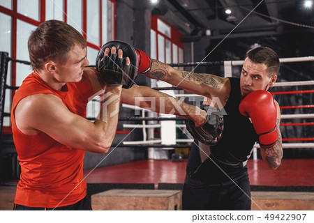 Counter punch. Strong tattooed athlete in sports clothing training on boxing paws with partner 49422907