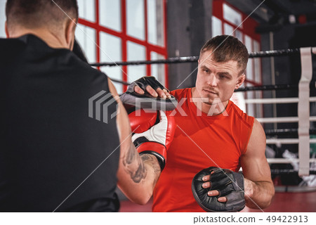 Close quarter boxing. Strong tattooed athlete in sports clothing training on boxing paws with 49422913