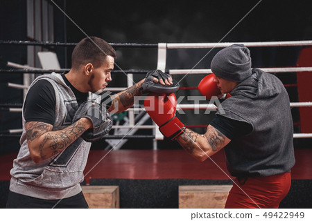 Good uppercut to the paw. Side view of muscular athlete in boxing gloves training on boxing paws 49422949