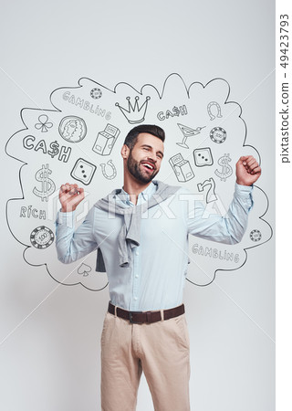 I won! Happy young man is celebrating his success with raised hands while standing against grey I won! Happy young man is celebrating his success with raised hands while standing against grey 49423793