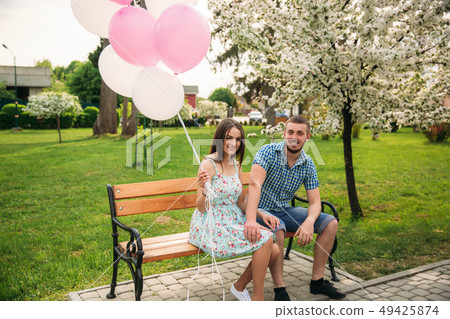 Couple siting on a bench and hold pink helium balls Couple siting on a bench and hold pink helium balls 49425874