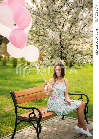 Girl sitting on a bench and hold pink helium balls Girl sitting on a bench and hold pink helium balls 49425877