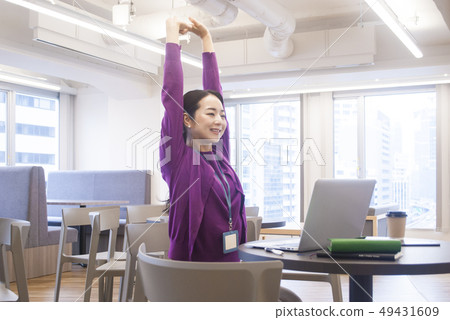 A woman stretching in front of a personal computer 49431609