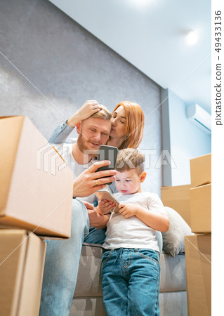 Young happy family with kid unpacking boxes together sitting on sofa 49433136