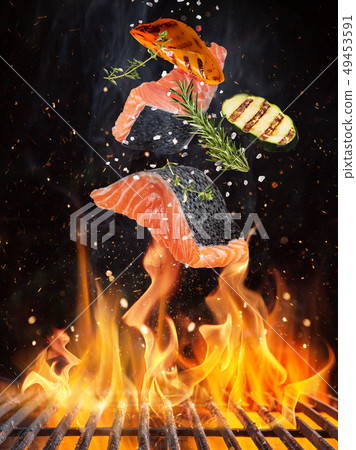 Tasty salmon steaks flying above cast iron grate with fire flames. 49453591