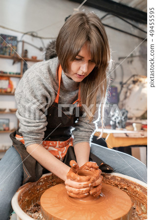 Happy woman working on potter wheel in pottery workshop. Family business shop sculpts pot from clay 49455595