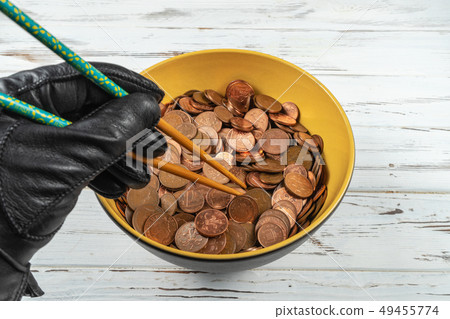 Bowl full of coins of the pound sterling and a hand holding chopsticks.Concept 49455774