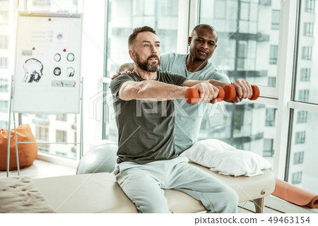 Concentrated handsome bearded male person lifting dumbbells 49463154
