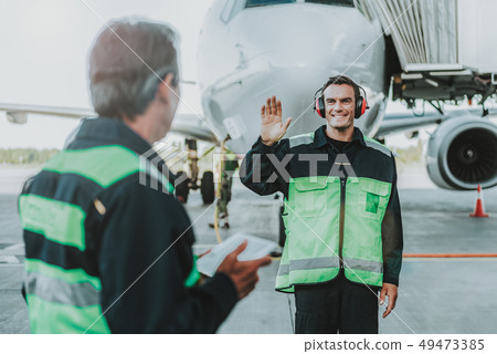 Smiling handsome employee in red headphone waving hands to mechanic 49473385