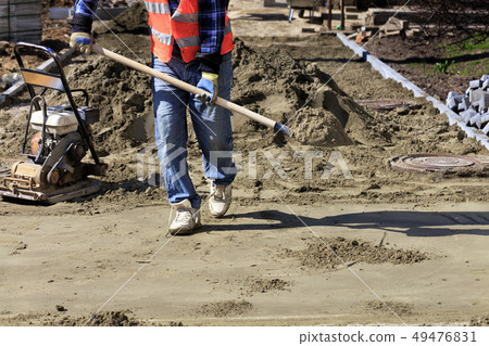 Laying tiles on the sidewalk, a worker carries 49476831