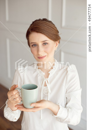 Attractive young woman in casual clothes is holding a cup, looking away and smiling, on white 49477754